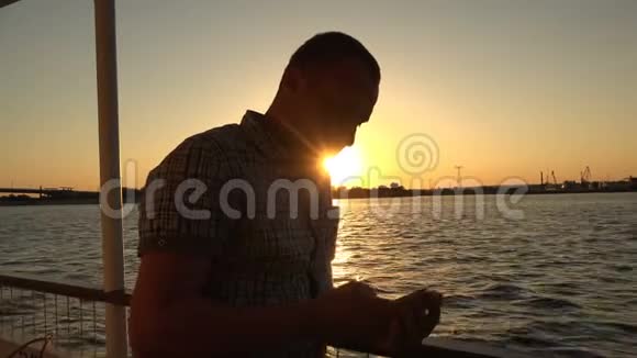 一个年轻人站在一艘机动船的甲板上看着电话视频的预览图