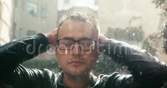 这位戴眼镜的帅哥在阳光明媚的日子里享受着雨的特写视频的预览图