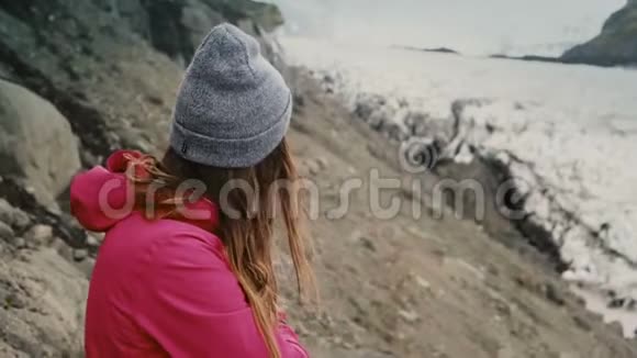 年轻的黑发女人站在山上看着冰岛瓦特纳霍卡尔冰湖的冰川视频的预览图