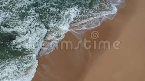 在葡萄牙金色沙滩上的蓝色海浪的平稳移动空中拍摄视频的预览图