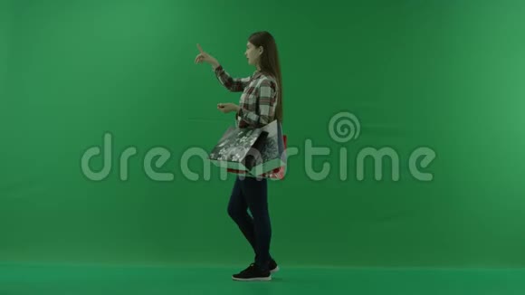 女孩站在她的左边带着包裹从绿色背景上的屏幕上选择一些东西视频的预览图