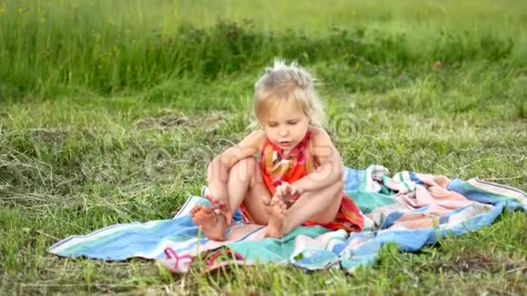 一个小金发女郎正坐在草地上的格子呢上视频的预览图