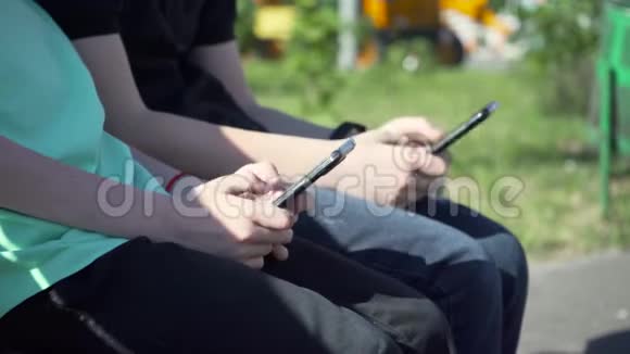 有黑色智能手机的男孩坐在长凳上带着手机的小男孩坐在花园里的长凳上儿童通过动员交流视频的预览图