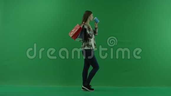 女孩站在她的右边肩膀上放着袋子在绿色的屏幕上喝着杯子里的东西视频的预览图