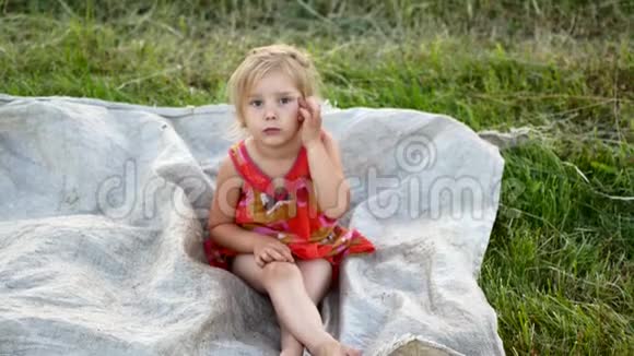 一个小金发女郎正坐在草地上的格子呢上视频的预览图