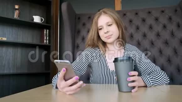 智能手机女孩在手机上使用应用程序在咖啡馆里微笑地喝咖啡美丽的年轻休闲女性专业手机视频的预览图