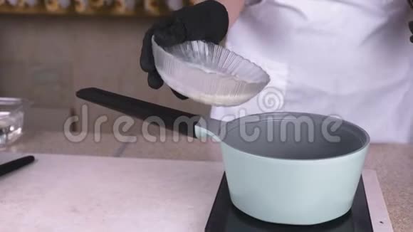 厨师把奶油从碗里倒入平底锅中再加热双手戴黑色手套特写视频的预览图