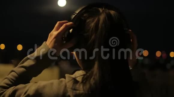 女孩戴上耳机晚上开始穿过城市月光下的运动员训练视频的预览图