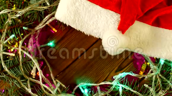 圣诞灯和云杉树枝在木制背景和红色圣诞老人帽子上2019年新年圣诞节一个视频的预览图