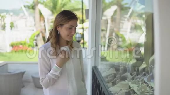 漂亮的年轻女孩看着相机要求一个男人在购物时在商店橱窗里买一件珠宝视频的预览图