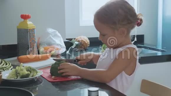 一个小女孩在家里的厨房里切布罗利做菜视频的预览图