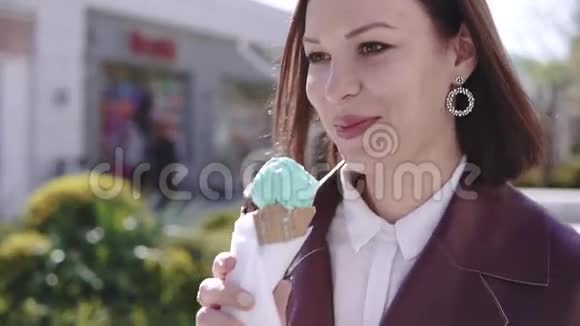 阳光明媚的日子里可爱时尚的黑发女孩走在百老汇大街上吃冰淇淋视频的预览图