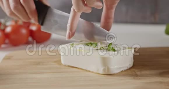 一个穿围裙的女人在白色厨房里用木切割板把一块软奶酪切成条做沙拉视频的预览图
