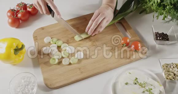 女人用一把刀在一张白色的厨房桌子上的木板上切下绿色韭菜做沙拉准备顶部视图视频的预览图