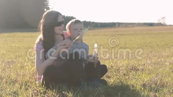 妈妈和儿子坐在草地上吹肥皂泡全家周末在公园视频的预览图