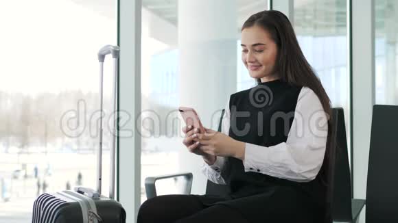 在机场候机楼等待航班时一位开朗的女商人在智能手机上发短信快乐的微笑女孩模特视频的预览图