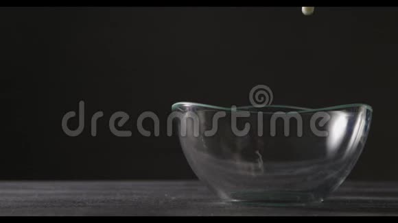 白牛奶倒在黑色背景上的玻璃碗里牛奶溅出灰桌上的碗视频的预览图