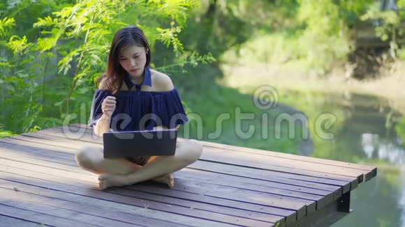 穿着紧身衣的女人在木制码头上用笔记本电脑视频的预览图