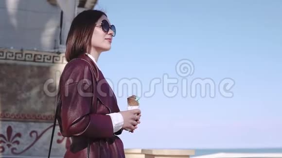 阳光明媚的日子里可爱时尚的黑发女孩走在百老汇大街上吃冰淇淋视频的预览图