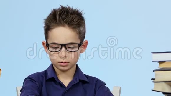 疲倦的男孩坐在桌子旁看书睡着了醒来蓝色背景关门视频的预览图