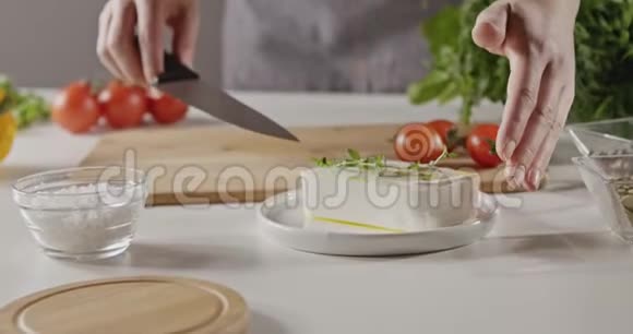 一个穿围裙的女人把一块软奶酪放在一个白色的餐桌上用于准备沙拉的木切割板上视频的预览图