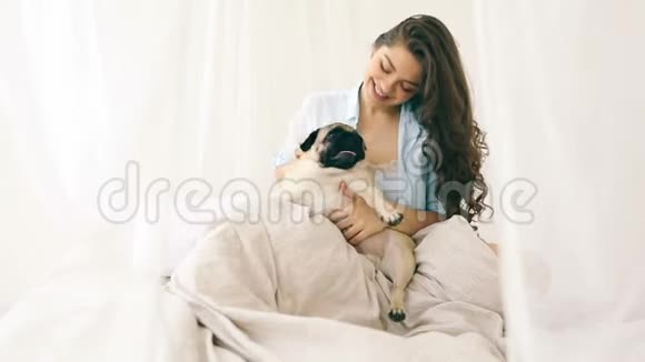 漂亮的女人穿着睡衣在床上玩她的狗录像片段日光灯视频的预览图