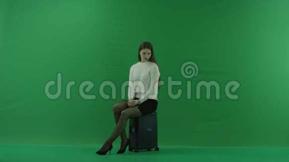 女孩一个女孩正坐在半转椅上坐在手提箱上看着绿色屏幕上的左边视频的预览图