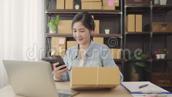 美丽的亚洲年轻企业家女企业家中小企业检查产品的股票扫描QR代码在家工作视频的预览图