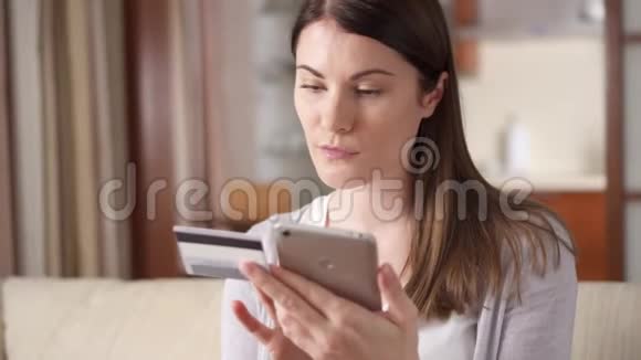女商人坐在客厅的沙发上用智能手机上网购买信用卡视频的预览图