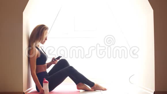 迷人的年轻女性做瑜伽和使用手机坐在地板上视频的预览图