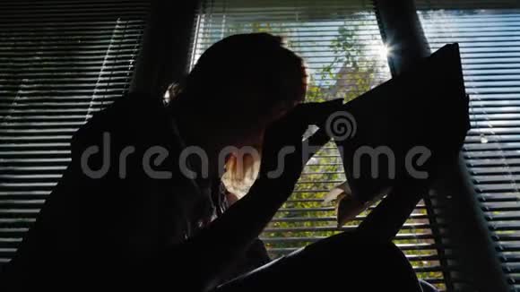 窗户边看书的女人的剪影阳光透过百叶窗明媚的春天视频的预览图
