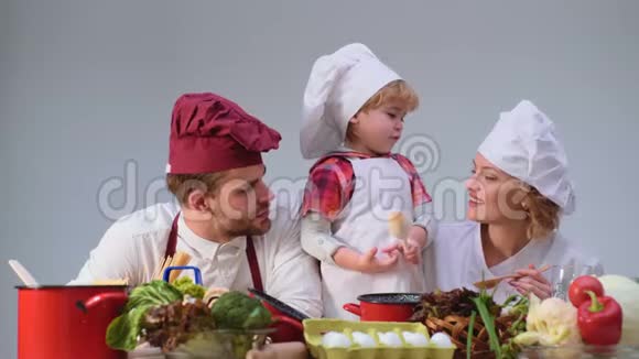 可爱的小男孩和他美丽的父母在厨房做饭时微笑年轻家庭在厨房做饭视频的预览图