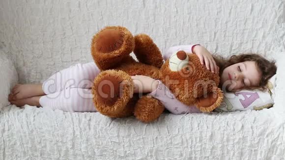一个小女孩拿着一只玩具熊在沙发上休息视频的预览图