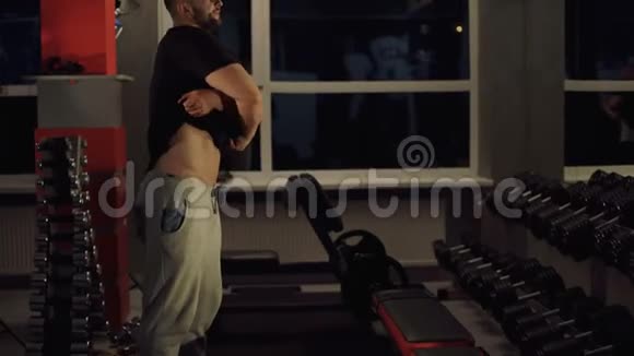 强壮的男人脱掉T恤在健身房休息时露出躯干视频的预览图