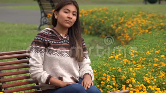 西班牙裔少女独自坐在公园长椅上视频的预览图