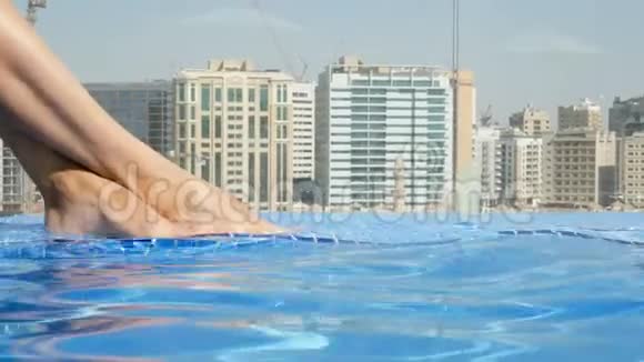 特写美丽的女性腿脚在屋顶游泳池与美丽的城市景观在摩天大楼的背景下视频的预览图