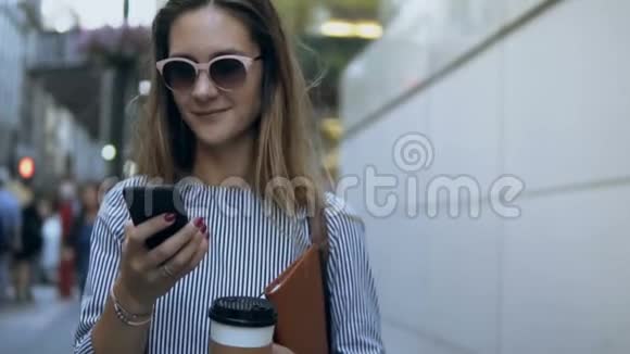 年轻漂亮的女商人拿着文件咖啡和智能手机走在街上的肖像慢动作视频的预览图