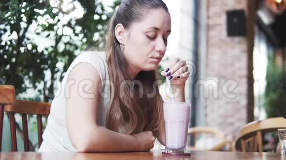 年轻漂亮的欧洲女孩在炎热的夏日在咖啡馆里喝着冰镇牛奶鸡尾酒和蓝莓妇女饮酒视频的预览图
