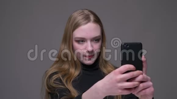 年轻迷人的黑发女性在手机上自拍的特写肖像背景与灰色隔离视频的预览图