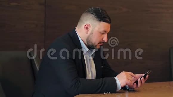 坐在餐桌上的胡子男在办公室里用手机视频的预览图