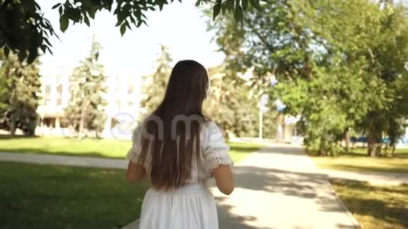 背着背包的女孩戴着耳机去公园听音乐微笑着十几岁的孩子高兴地挥手视频的预览图