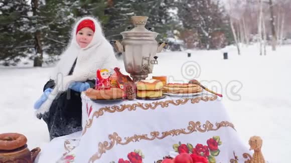 一个穿着裘皮大衣戴着俄罗斯风格围巾的小女孩坐在节日的餐桌旁扮演着一个俄罗斯的马崔什卡视频的预览图