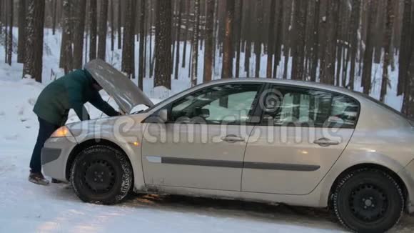 冬天一个人修理一辆破汽车一名男子站在打开的汽车引擎盖旁正在寻找破损处视频的预览图