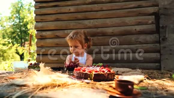 可爱的小男孩穿着白色皮条在户外的餐桌上吃水果蛋糕和牛奶视频的预览图