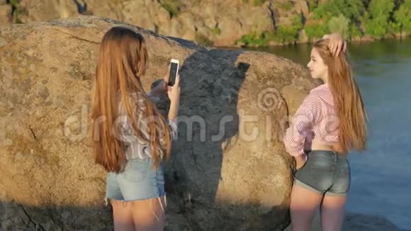 两个年轻的女朋友带着智能手机在岩石上视频的预览图
