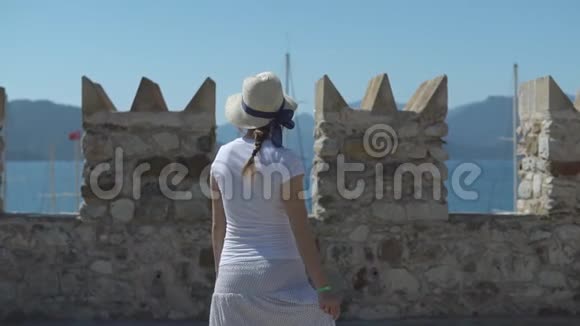 阳光明媚的夏日戴着帽子的年轻漂亮女孩在石堡上旋转旋转视频的预览图