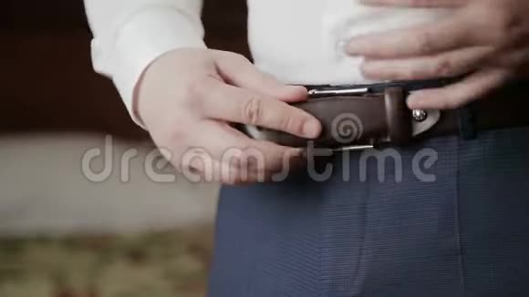 新郎在婚礼的早晨把腰带系在裤子上视频的预览图