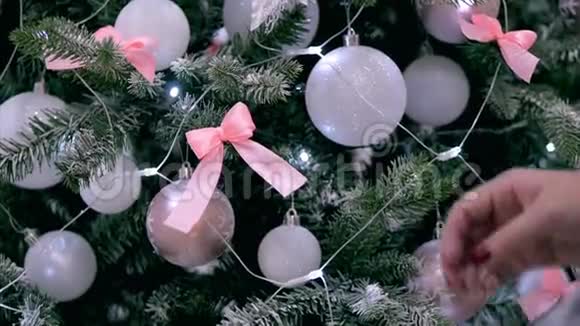 年轻女子的双手在圣诞树上展开一个蝴蝶结用节日的灯光和视频的预览图