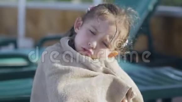 一个小女孩裹着毛巾脸很脏孤独地坐在游泳池旁的一个阳光休息室里视频的预览图
