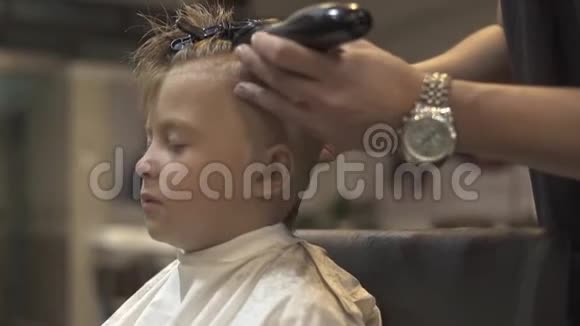 儿童理发店用电动剃须刀理发的小男孩画像使用电动剃须刀的发型师视频的预览图